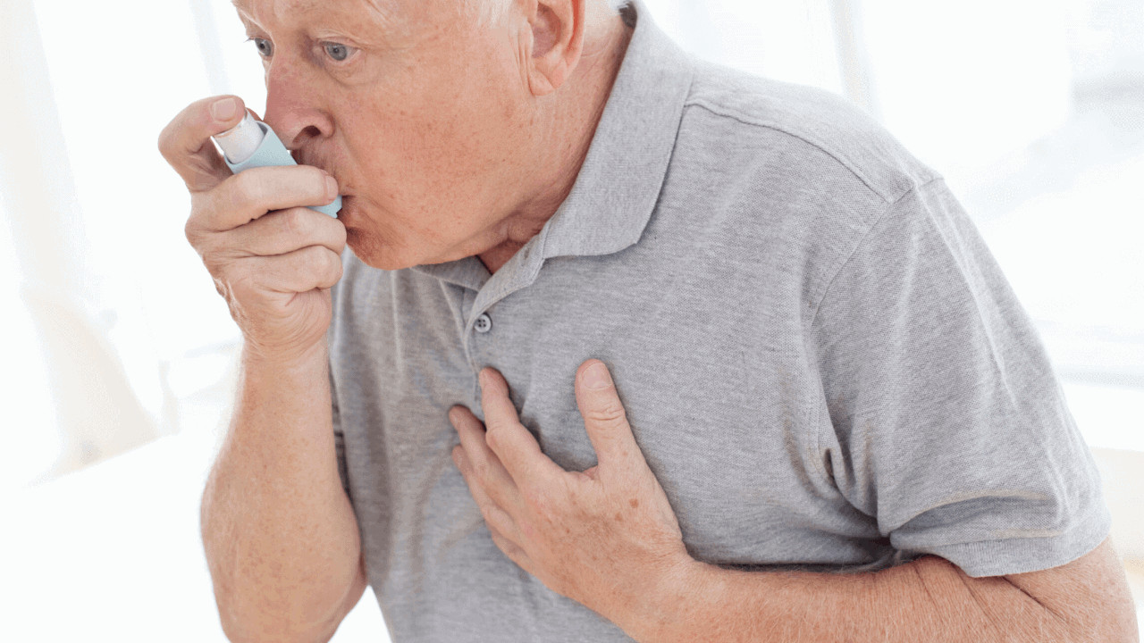 A man uses an asthma puffer while clutching his chest